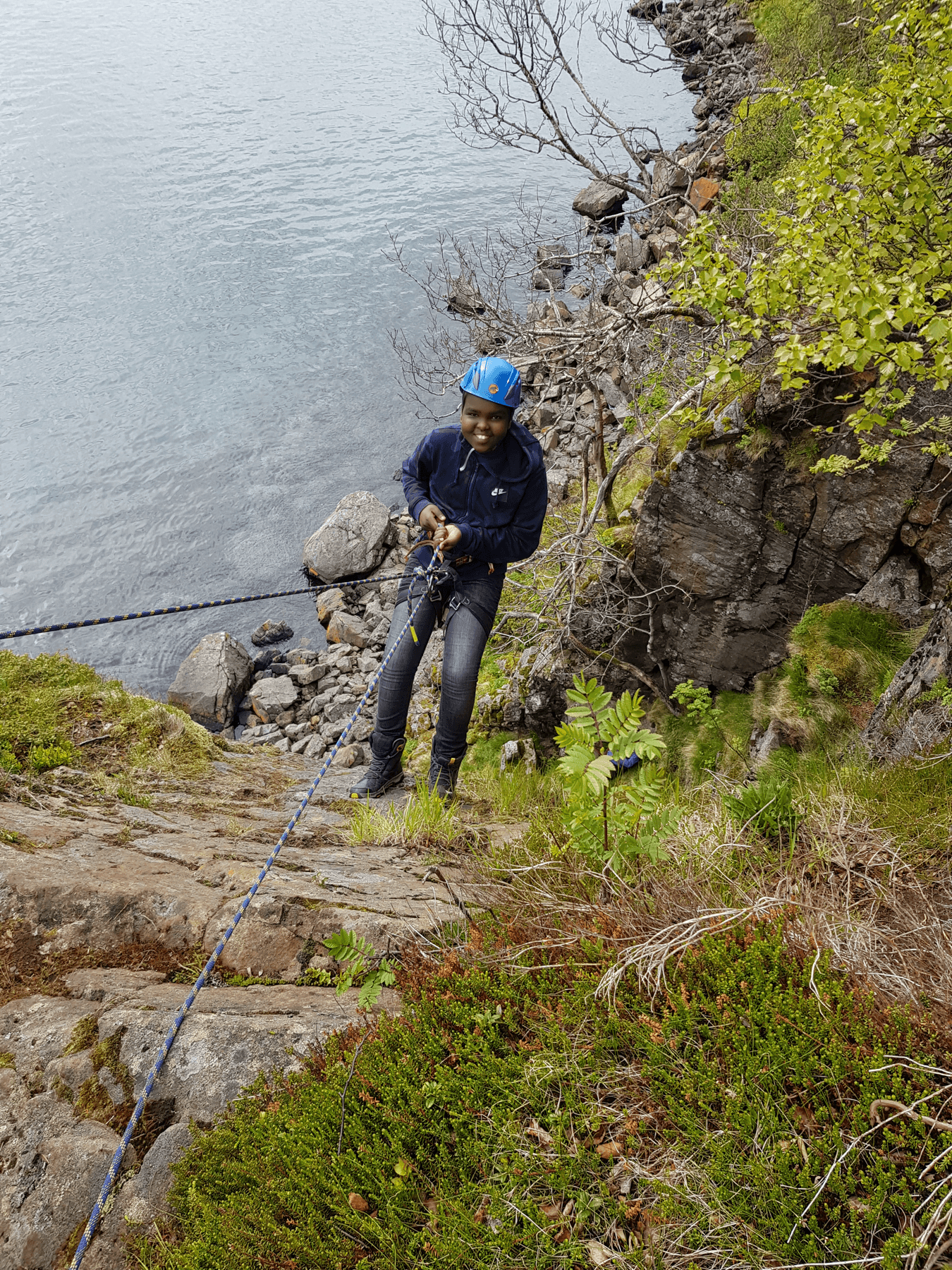 Smilende jente rappellerer ved fjellkant over hav