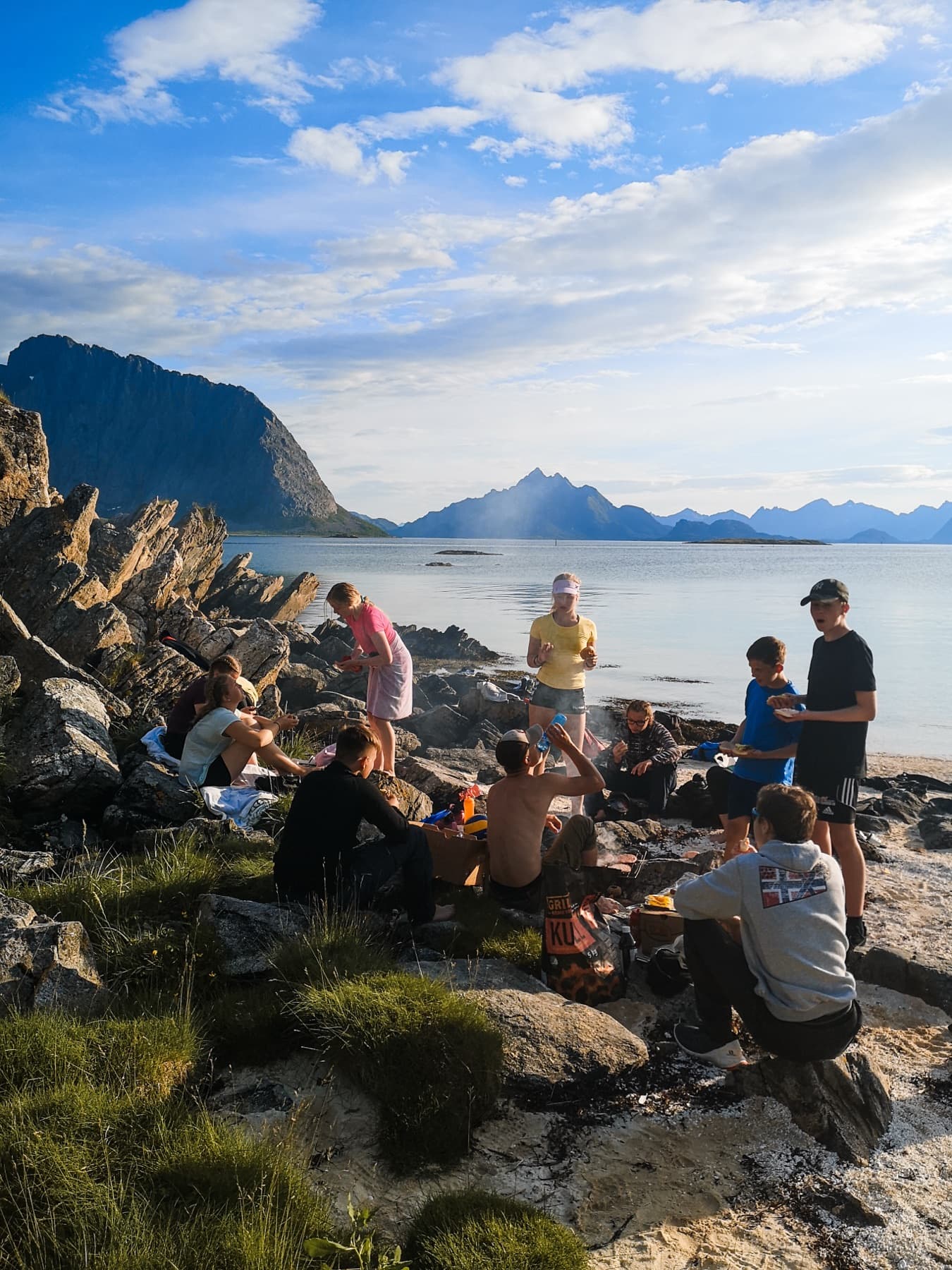 Tenåringer rundt bål på steinete strand i kveldslys